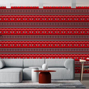 Swazi inspired wallpaper red background with geometric repeat pattern of zig zag lines and shield and spear graphics and oval shapes in colours black and white. Setting is a living room with a corner sofa that complement the wallpaper.