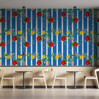 Coffee shop setting with chairs and tables. On the wall is a Tsonga inspired wallpaper. Wallpaper pattern of a colourful floral pattern of yellow flowers and red flowers with green leaves, on a background of blue and white vertical stripes.