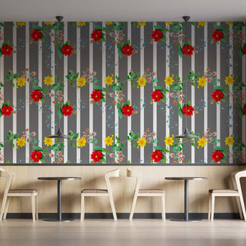 Coffee shop setting with chairs and tables. On the wall is a Tsonga inspired wallpaper. Wallpaper pattern of a colourful floral pattern of yellow flowers and red flowers with green leaves, on a background of grey and white vertical stripes.
