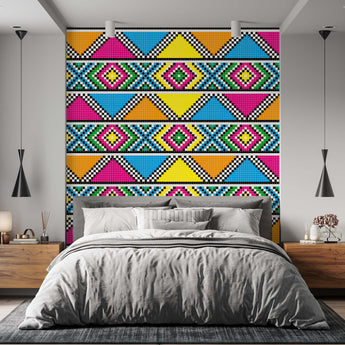 On a wall is a Zulu inspired wallpaper with a geometric repeat pattern of triangles and diamond shapes. Colours pink, orange, blue, black and white. Setting is a bedroom with a bed and wooden pedestals